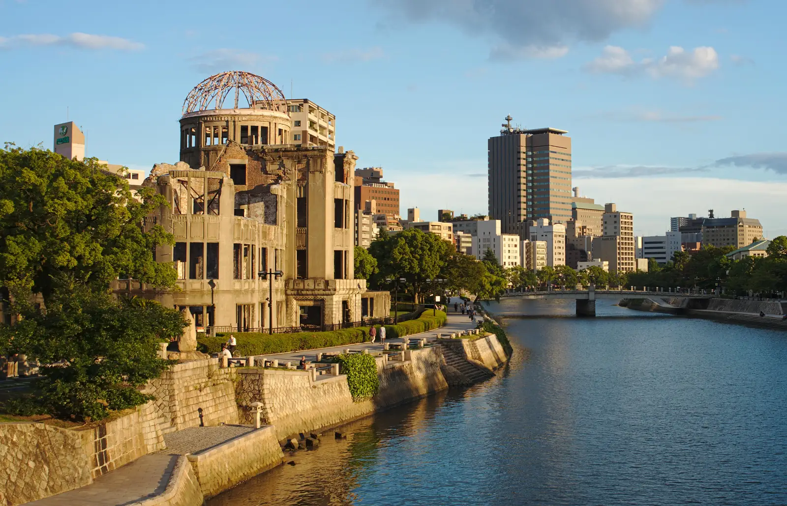 The Atomic Bomb Dome in warm evening light beside the Motoyasu River, with the riverside walk and city buildings around it