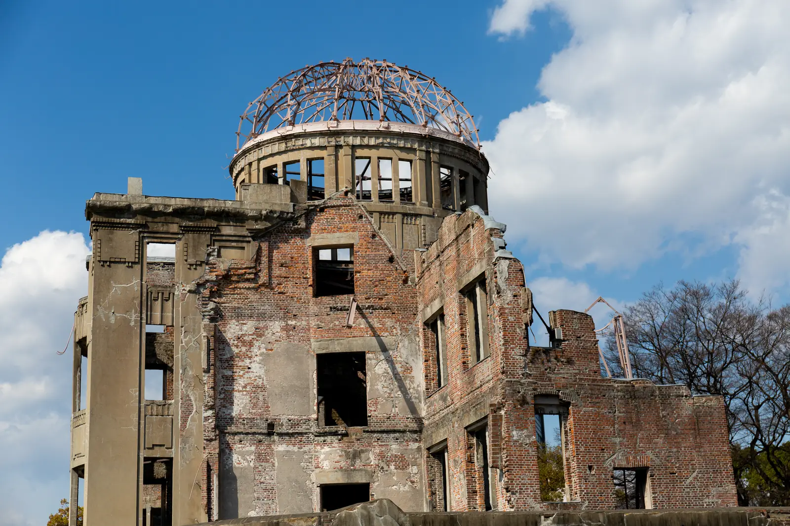 Close view of the bare steel frame of the dome on top of the ruined brick and stone walls, against a blue sky with white clouds