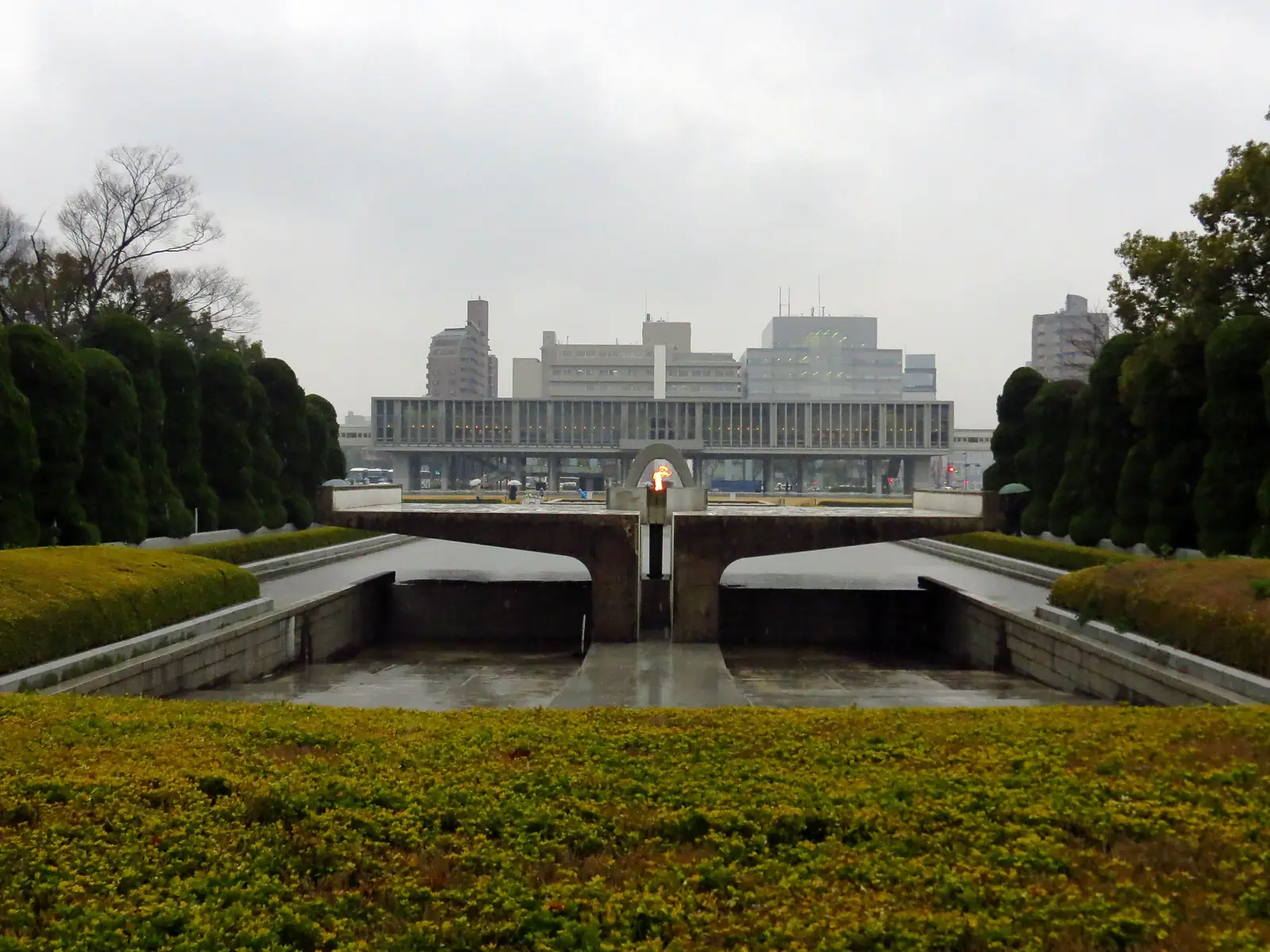 The Flame of Peace burning on its pedestal in the Pond of Peace, the museum behind it