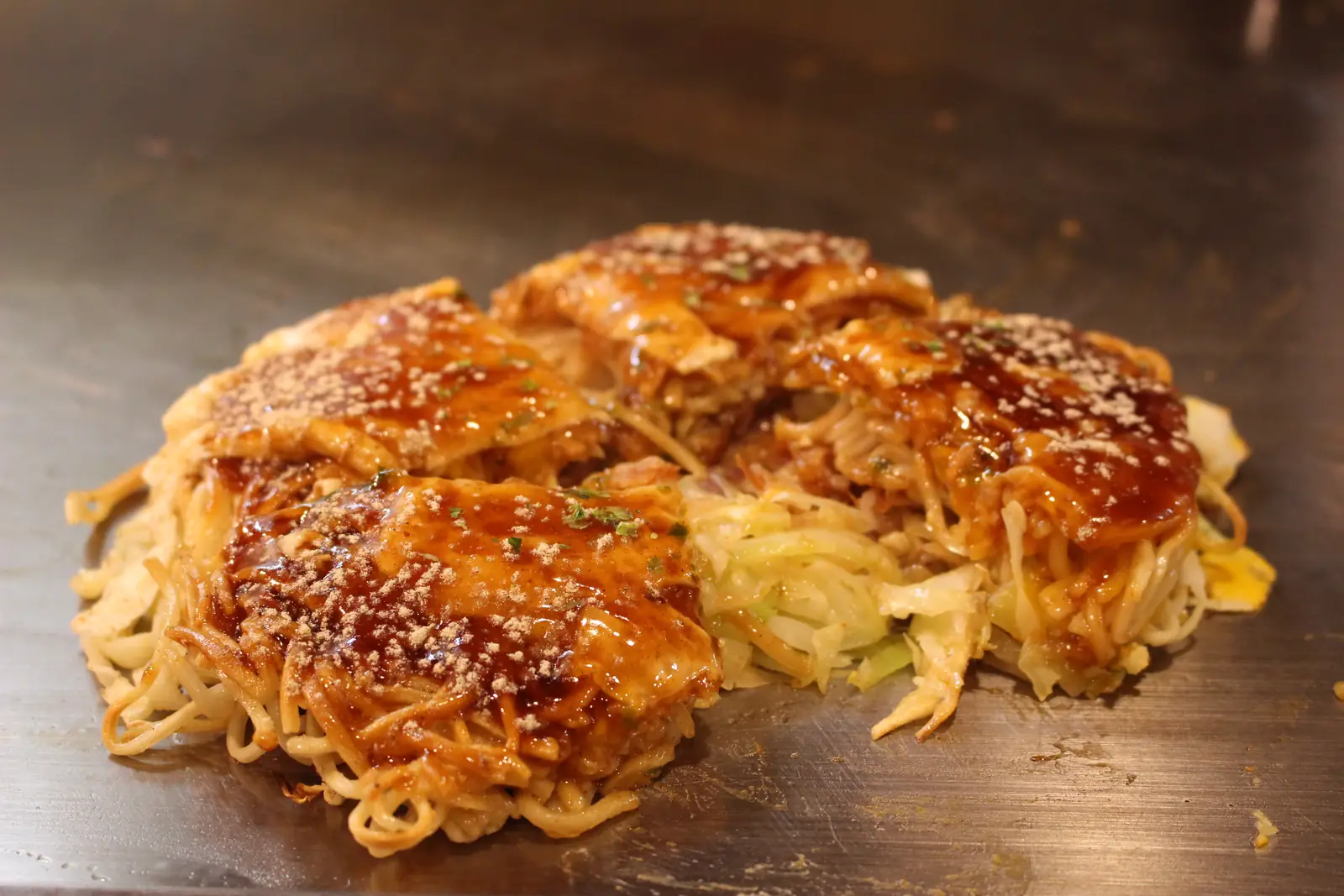 A Hiroshima-style okonomiyaki with noodles and cabbage, glazed with sauce and sesame