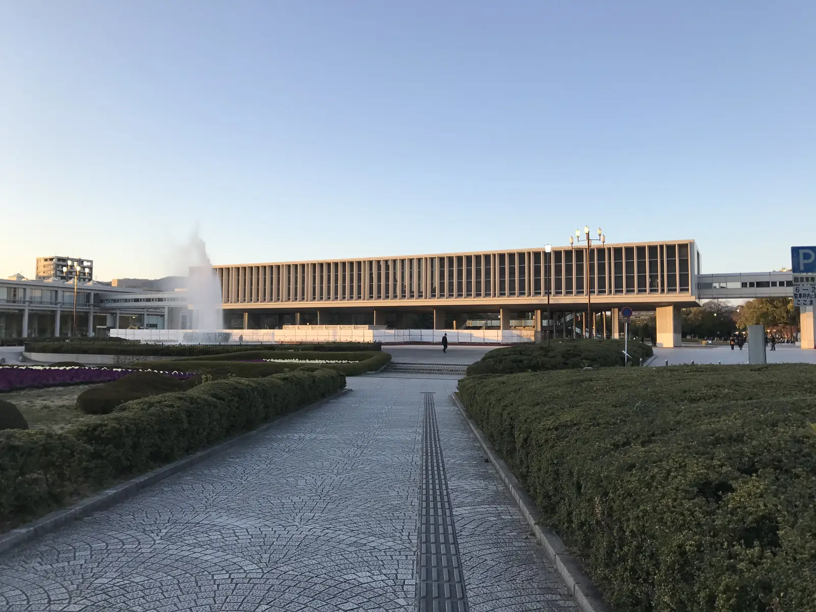 The long, low Peace Memorial Museum building raised on pillars at the end of a paved path, with a fountain and hedges in front