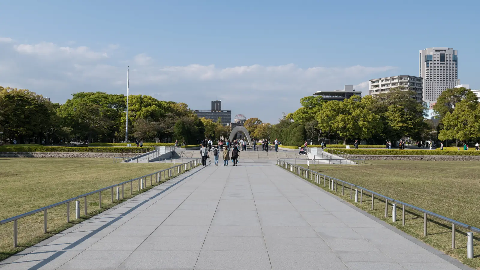 A wide paved path across the lawns of Peace Memorial Park leading to the Cenotaph, with the Atomic Bomb Dome small in the distance